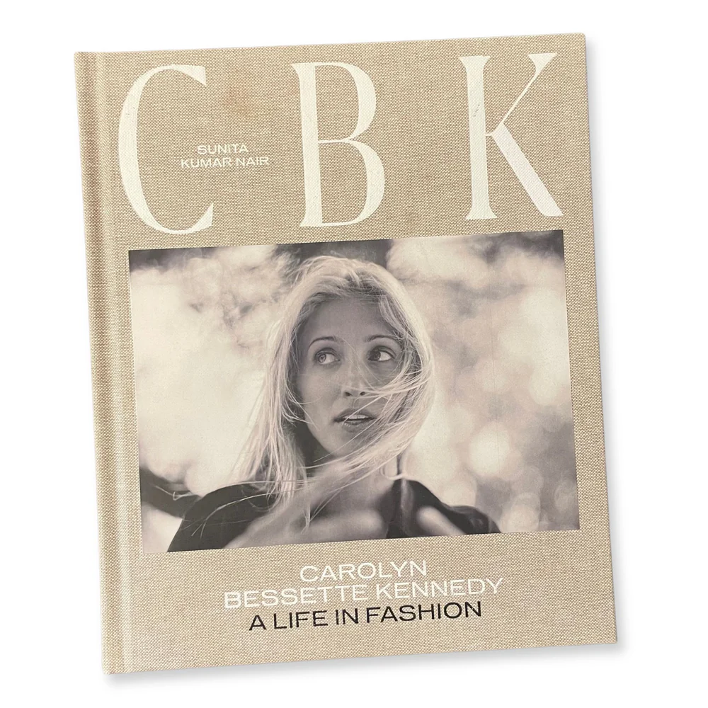 Book cover of CBK featuring a black and white portrait of Carolyn Bessette Kennedy with windswept blonde hair, against a beige linen-textured background