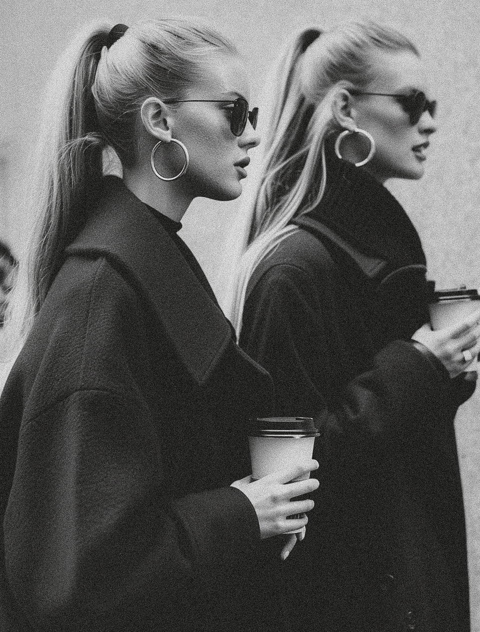 Black and white photo of stylish woman in black coat holding coffee cup, main character energy