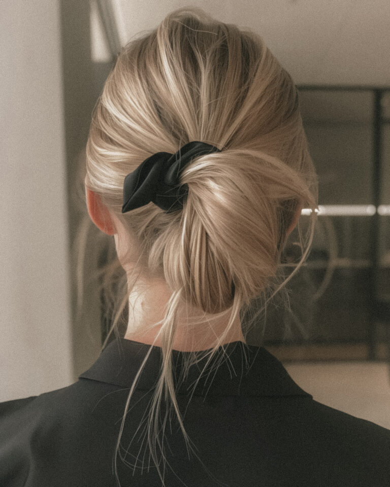 Woman embodying manifestation success through intentional style, wearing black blazer with blonde hair in elegant messy bun, photographed from behind